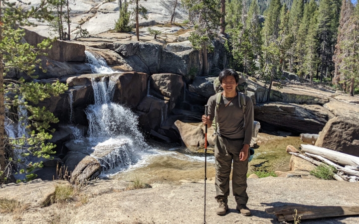 a student poses beside a waterfall on a high sierra backpacking course for bipoc